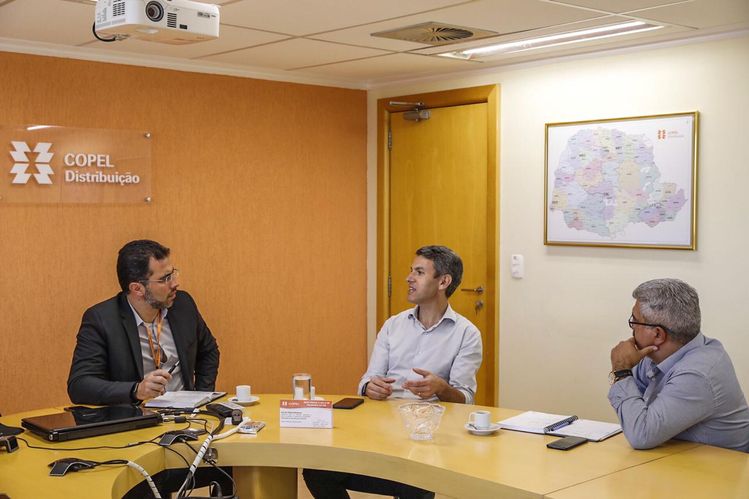 Gilson sentado na mesa com representantes da Copel conversando.