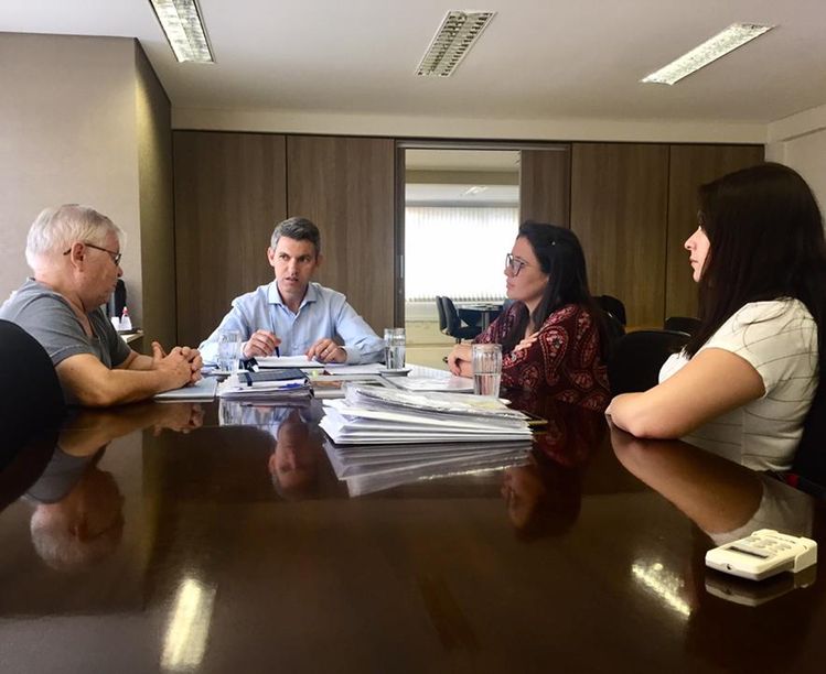 Foto do presidente da COmec gilson santos em seu gabinete sentado na mesa com a secretaria de pien e sua assistente