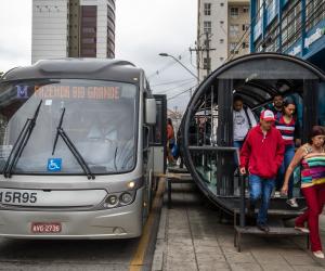 Foto de ônibus parado ao lado do tubo com pessoas desembarcando 